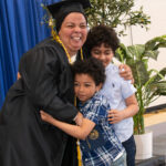 a woman wearing cap and gown hugs two children