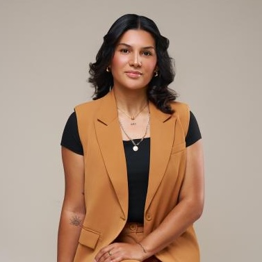 Photo of Kisleiny sitting on a pale backdrop smiling at the camera