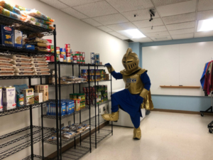 NECC Knight mascot stands in the food closet looking at the dry goods.