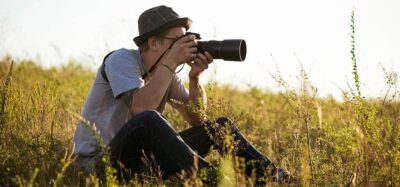Intro to Photography - a photographer sitting in the grass with a camera pointed at a subject, sunny day